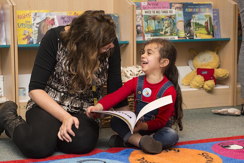 A woman and young girl laughing while reading a picture book